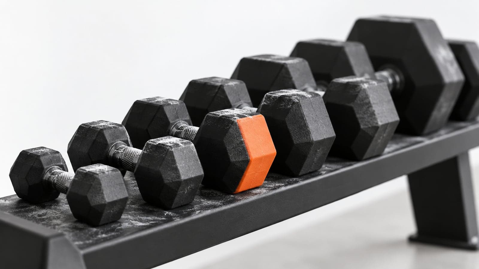 Row of matte black dumbbells on a rack with one orange-capped pair in the middle