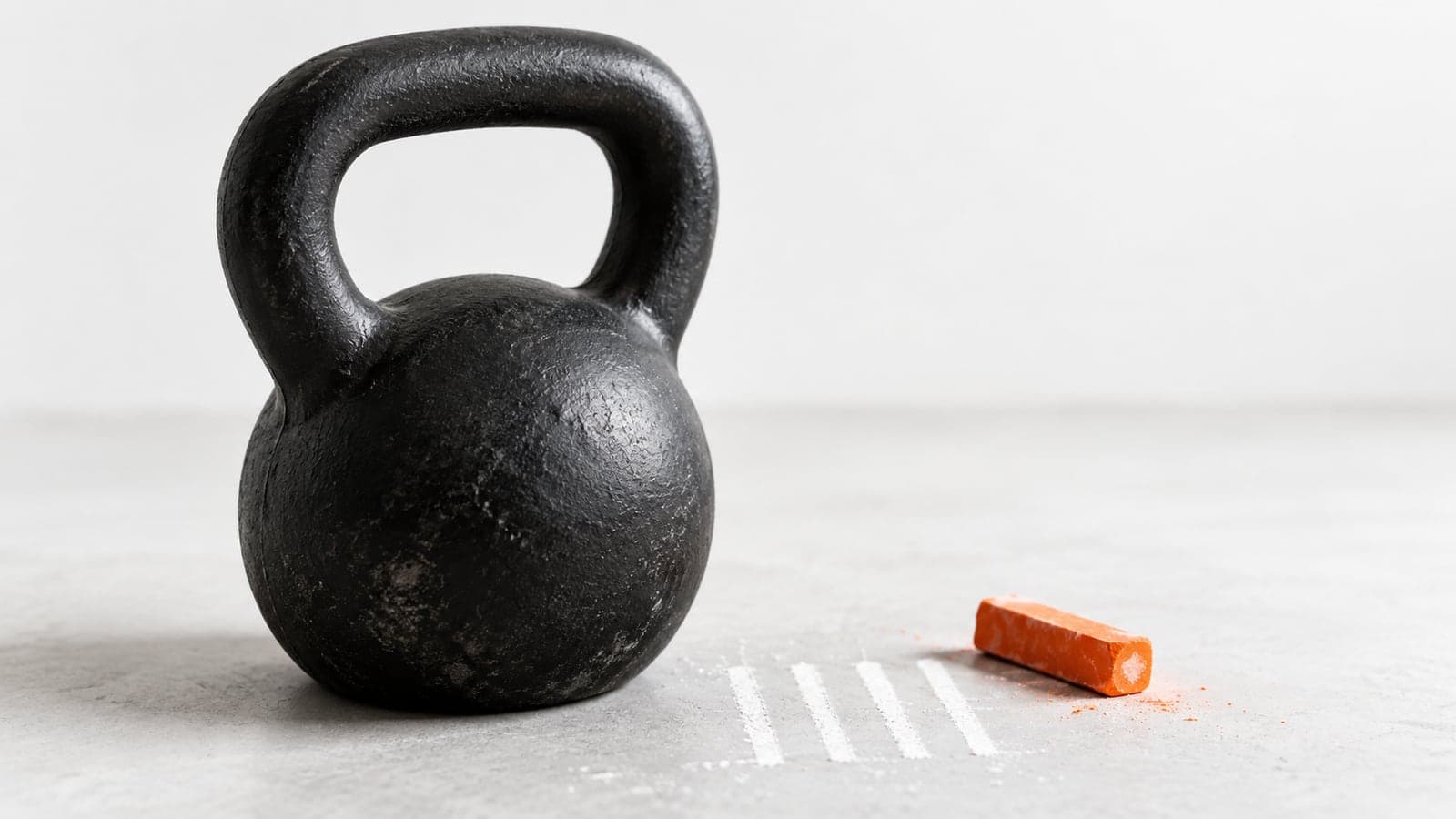 Row of matte black dumbbells on a rack in a bright studio, one pair with an orange handle