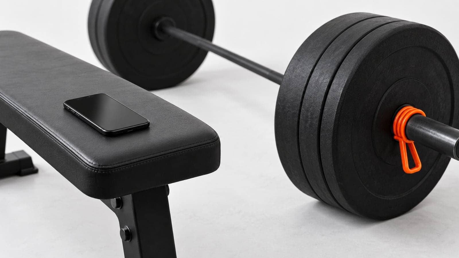 A phone resting on a flat bench beside a loaded barbell