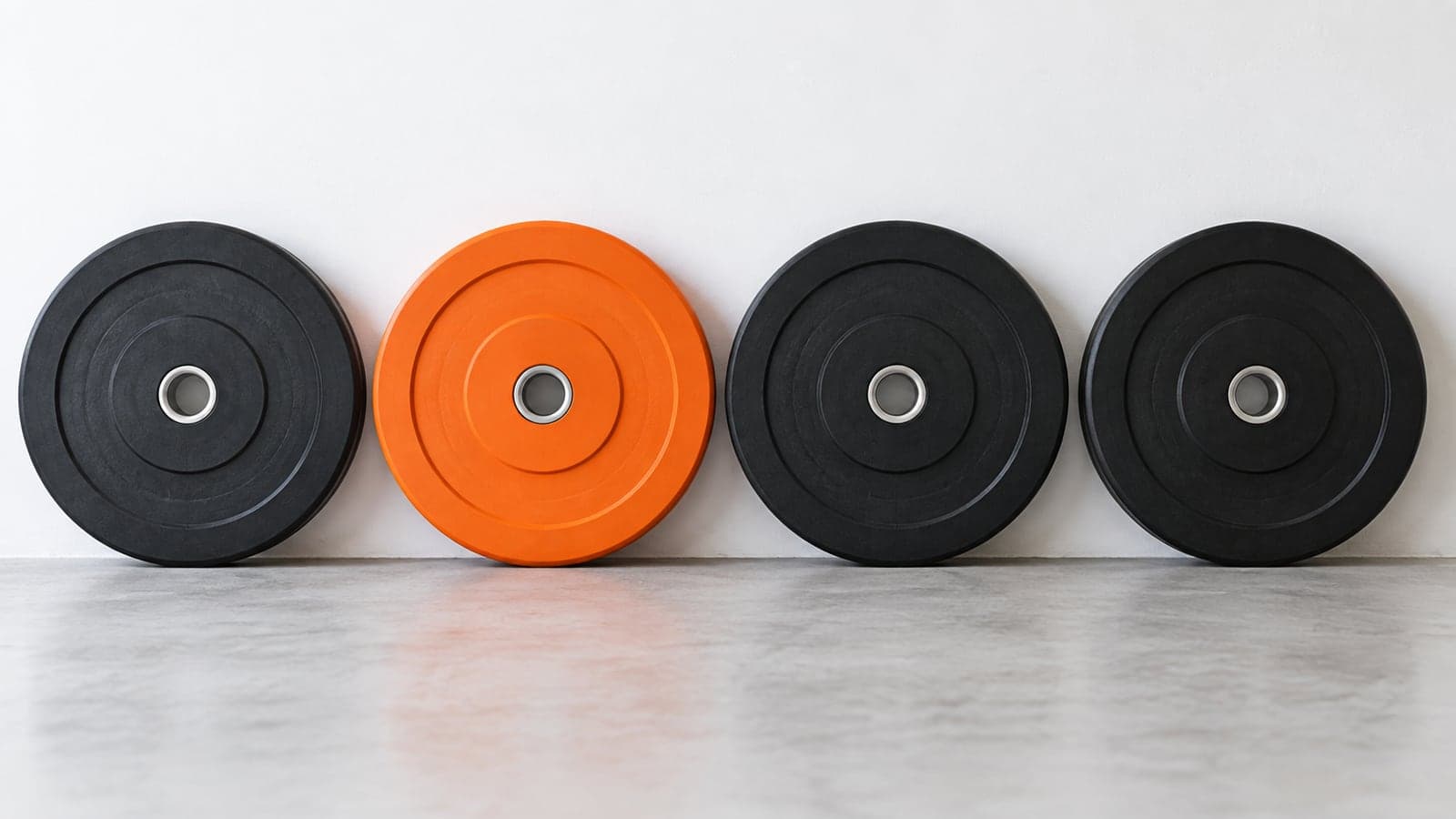 Loaded barbell resting in a matte black squat rack in a bright studio, one orange collar on the sleeve