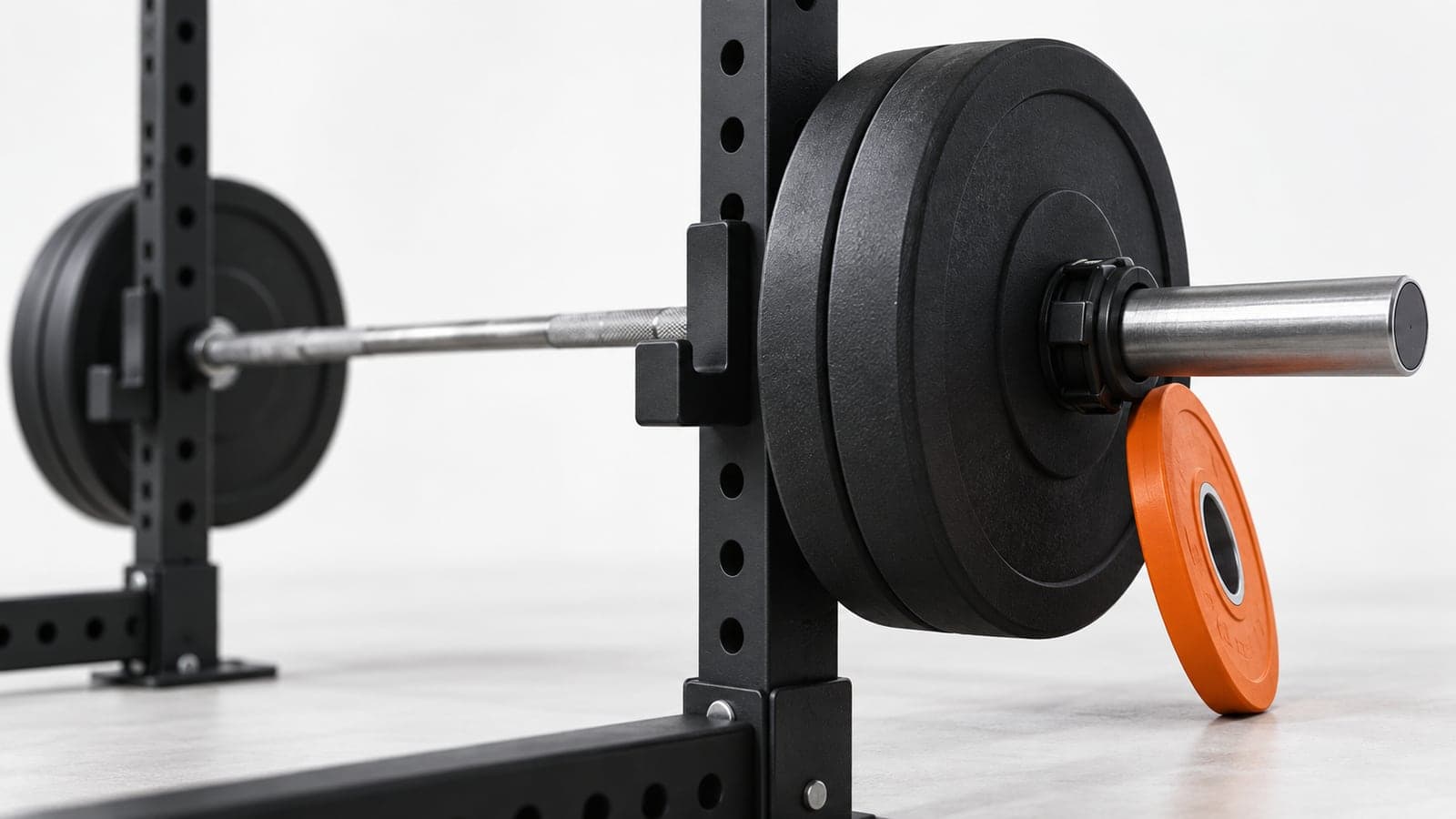 Loaded barbell resting in a bench press rack with one small orange weight plate on the end